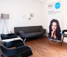 Ansicht Wartezimmer mit schwarzen Sofas und Aufsteller